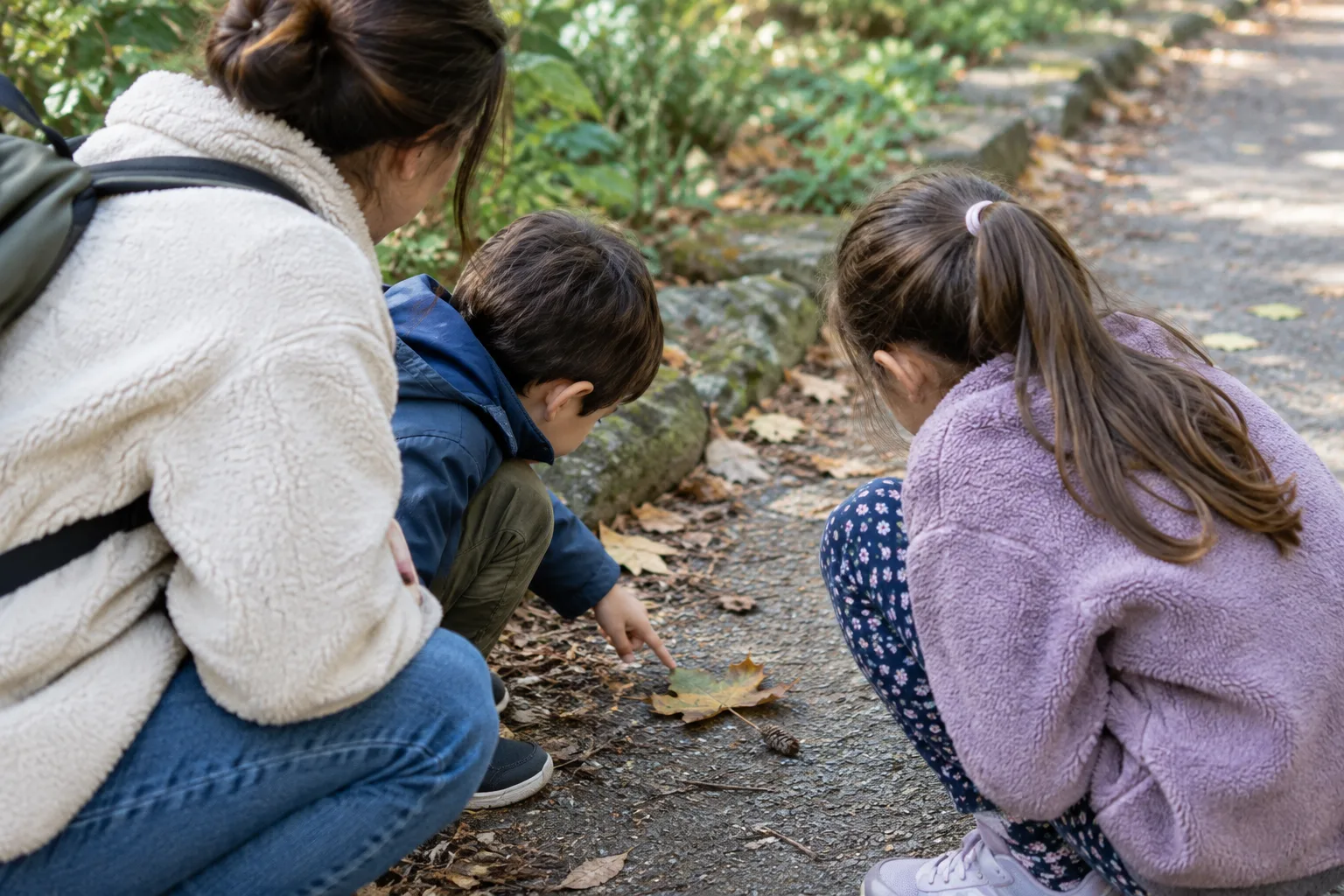 Un parent et deux enfants observent une feuille au bord d’un chemin.